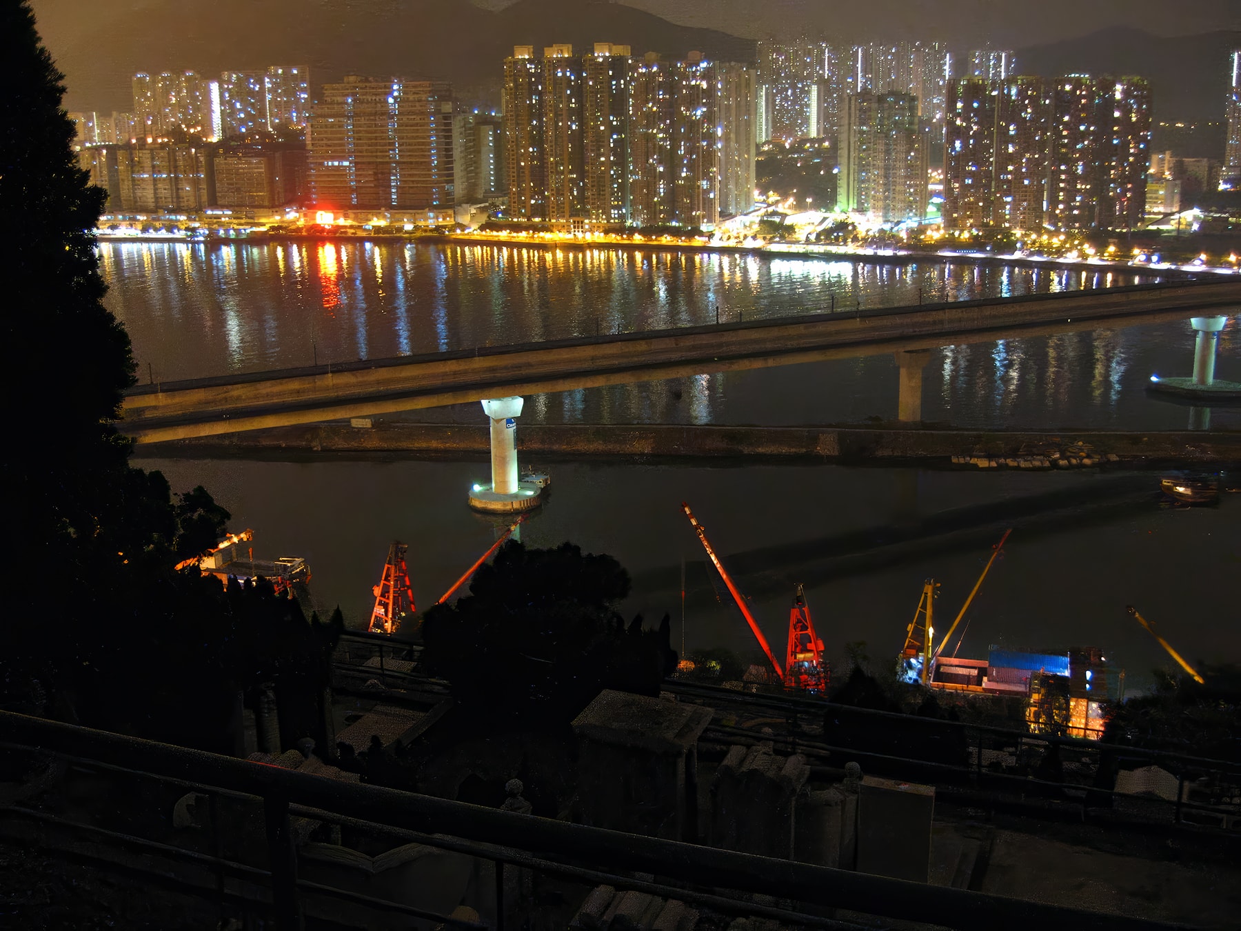 Cemetery in foreground with illuminated Hong Kong skyline and bridge at night