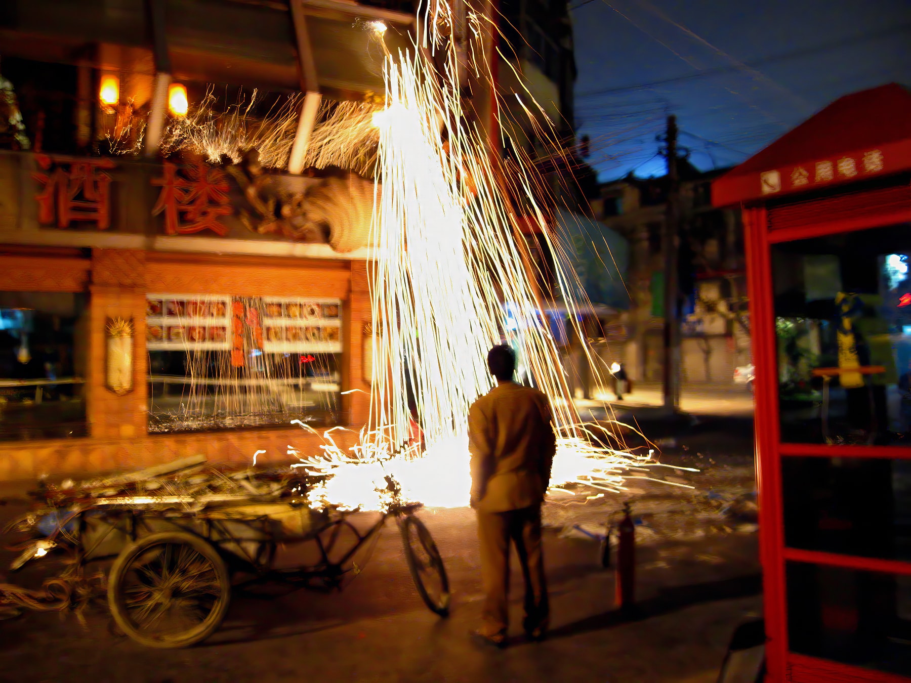 Man watching street fireworks explode outside restaurant at night, Shanghai