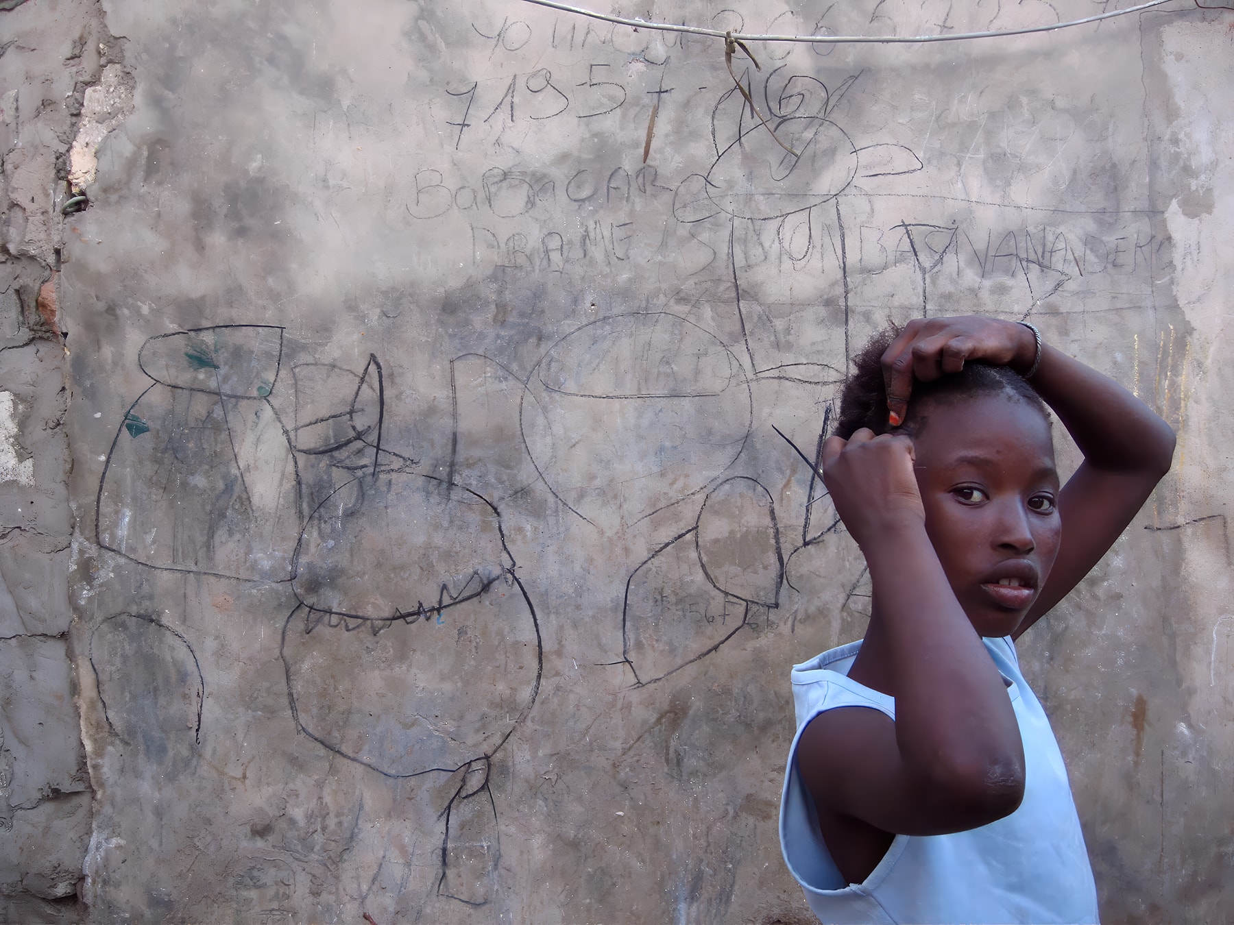 Girl in front of wall with chalk drawings, Dakar