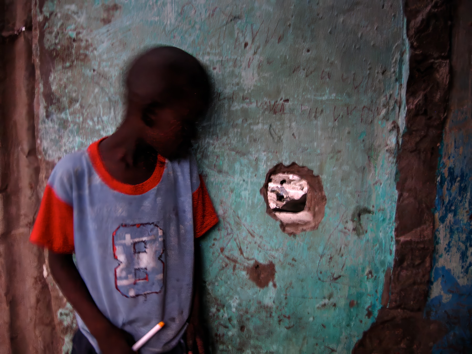 Boy leaning against teal wall with hole, Dakar