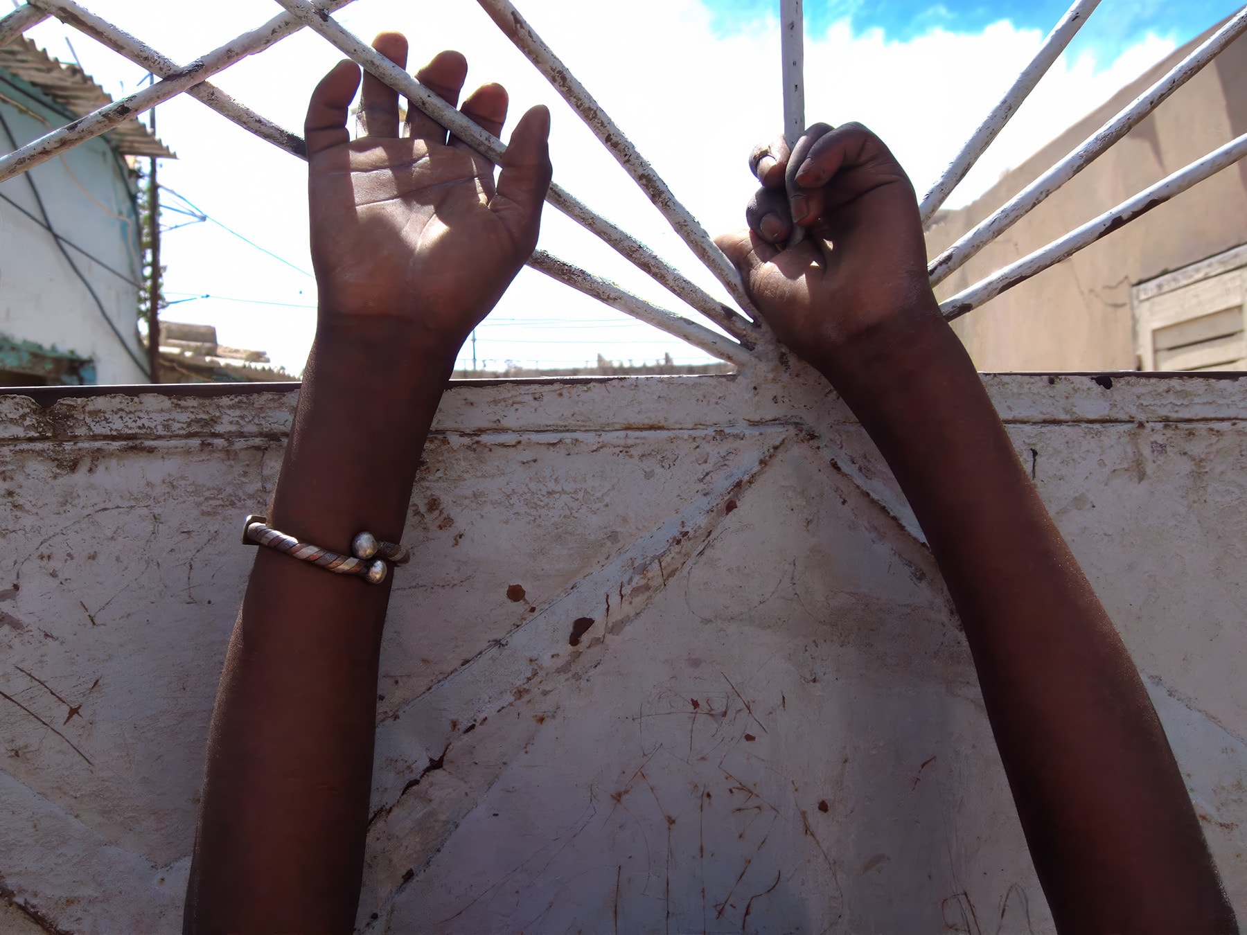 Hands gripping iron gate against sky, Dakar