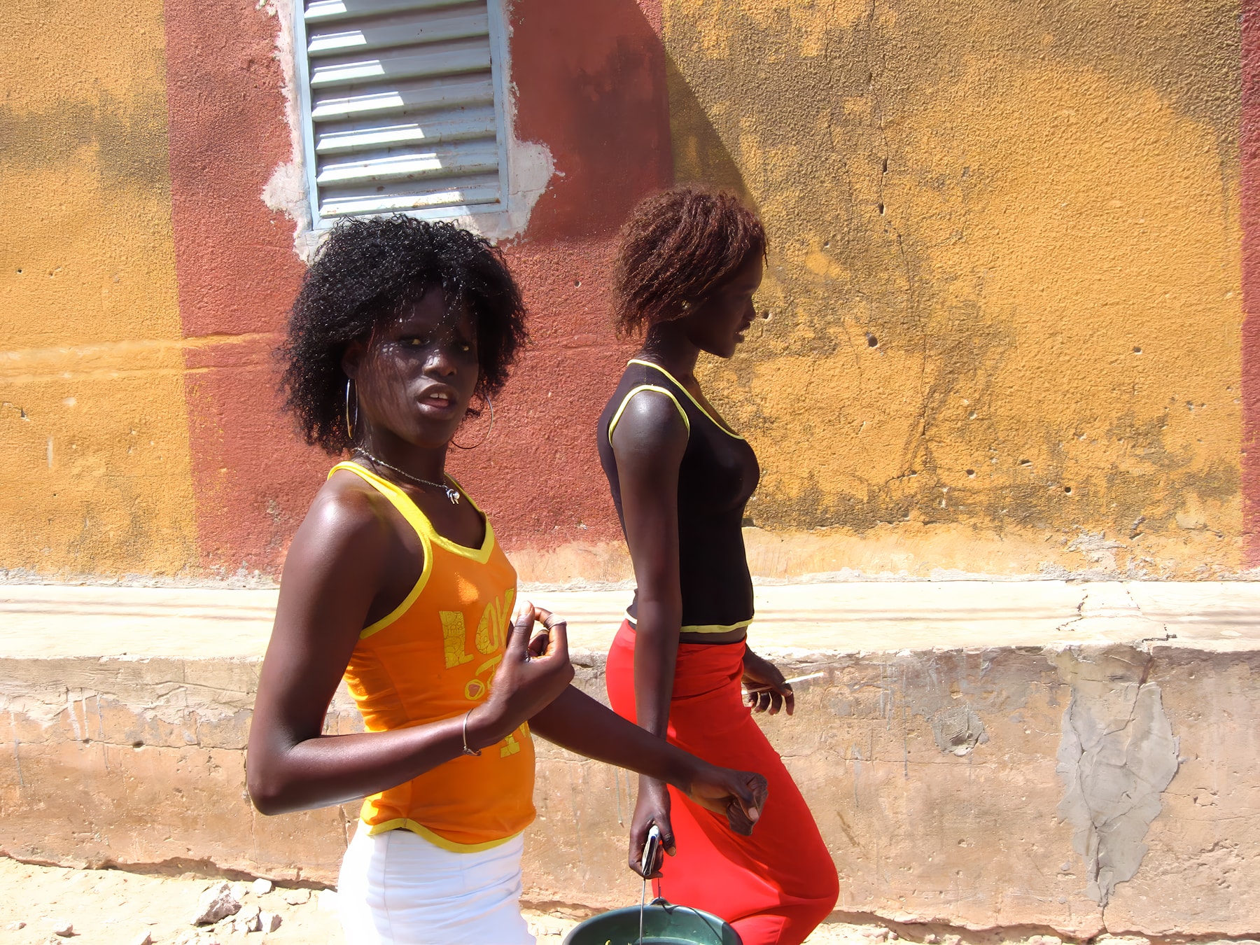 Two women against a yellow and red wall, Senegal